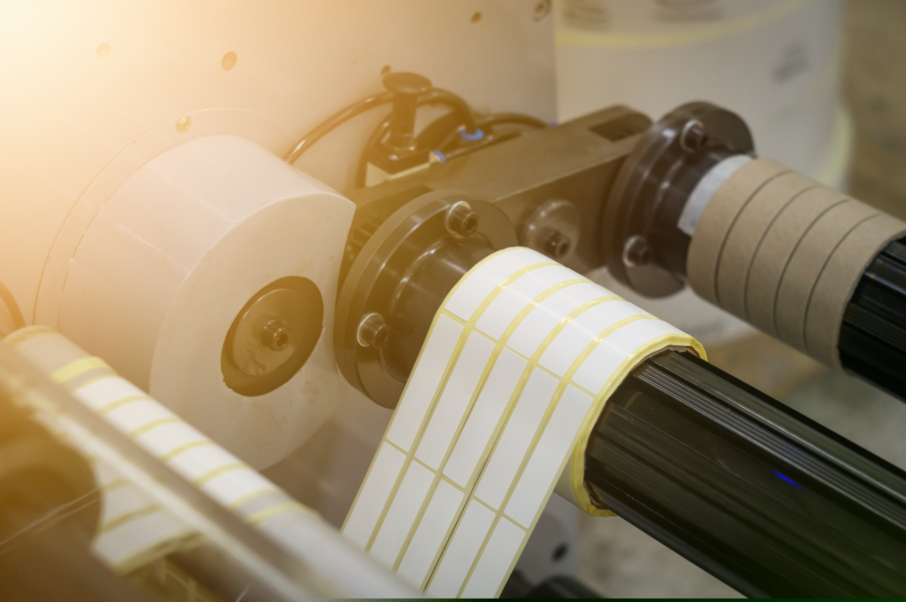 A machine for the production of white self-adhesive labels. The shafts of the machine for winding rolls of tape with a label. Die-cutting and cutting of paper for label production. Selective focus